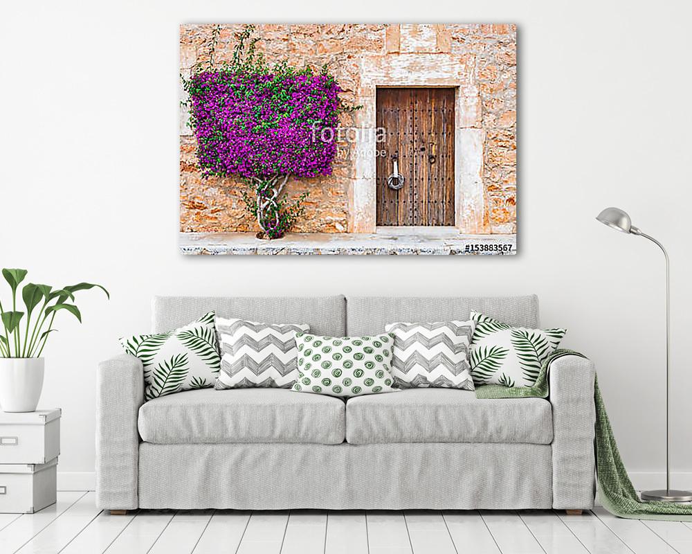 Old wooden door and stone wall with mediterranean bougainvillea (poszter) - vászonkép, falikép otthonra és irodába